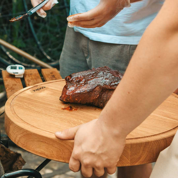 Hackbrett aus Holz Natur, Rund Größe M, mit Griffeinkerbung, Milieubild im Garten, Steak liegt auf Brett