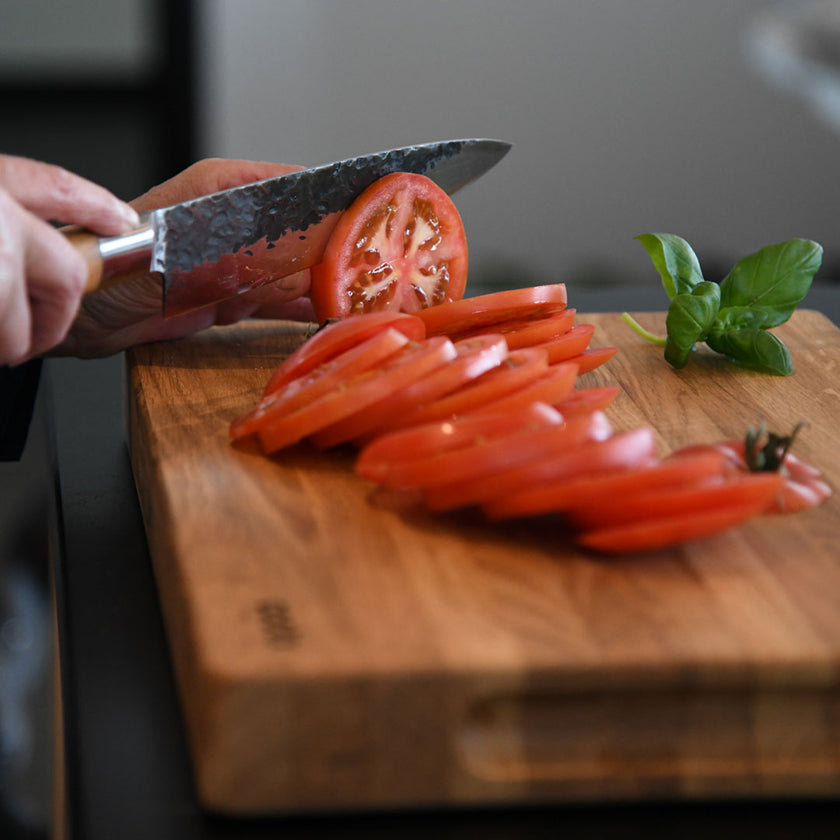 Hackbrett aus Eichenholz Natur, Größe M, COOKX Logo unten rechts eingraviert, Milieubild in Küche, Tomate wird auf Brett geschnitten