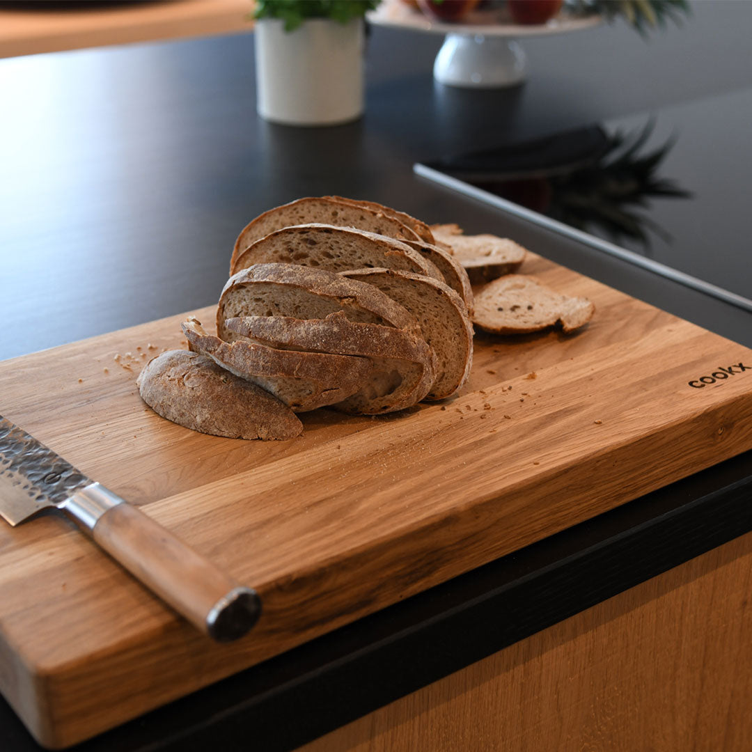 Hackbrett aus Eichenholz Natur, Größe M, COOKX Logo unten rechts eingraviert, Milieubild in Küche, auf Brett liegt geschnittenes Brot und ein Messer