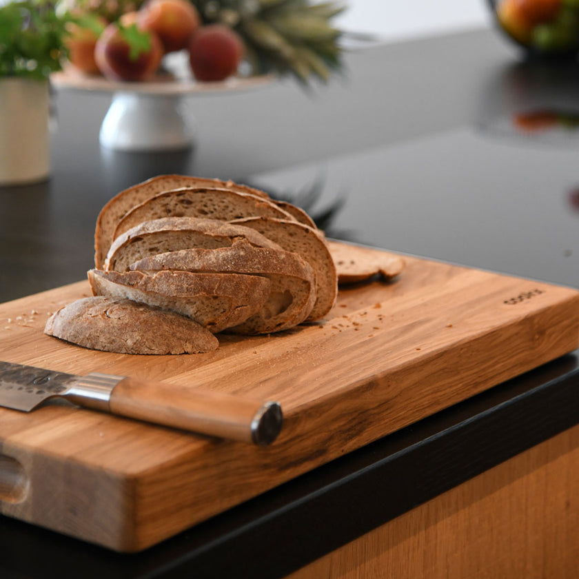 Hackbrett aus Eichenholz Natur, Größe S, COOKX Logo unten rechts eingraviert, Milieubild in Küche, auf Brett liegt geschnittenes Brot und ein Messer