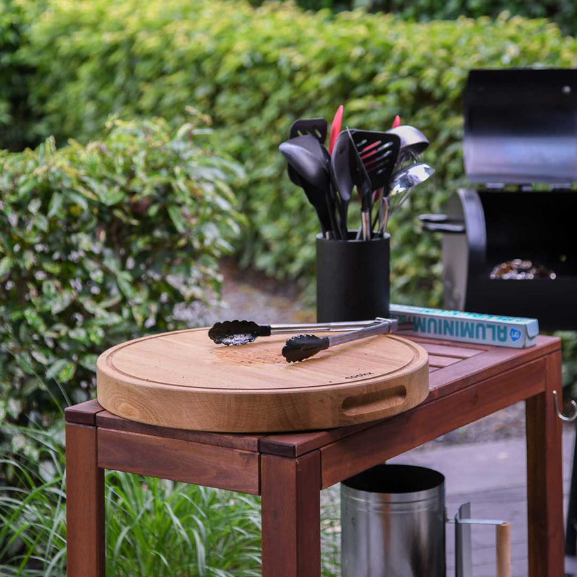 Hackbrett aus Holz Natur, Rund Größe M, mit Griffeinkerbung, Milieubild im Garten, Zange liegt auf Brett