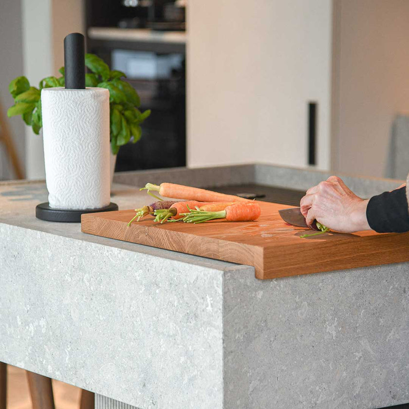 Hackbrett aus Eichenholz, Antirutschkante, hochkant 34 x 50 x 3,5 cm, rechts unten Logo von COOKX eingraviert, Milieubild in Küche, Brett liegt auf Kücheninsel, Karotten auf Brett geschnitten, Ansicht seitlich