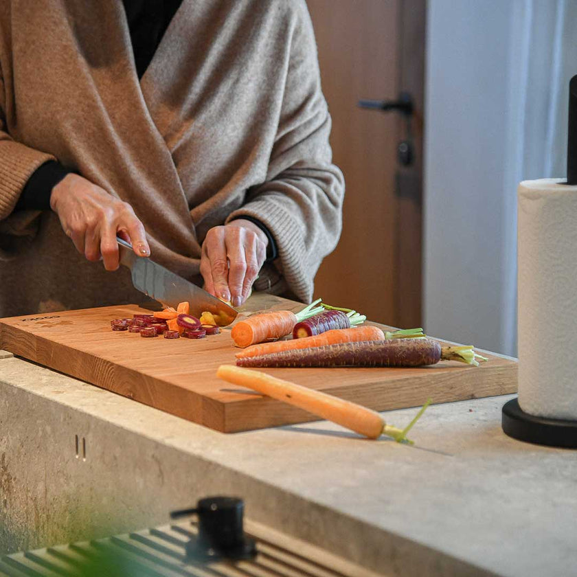 Hackbrett aus Eichenholz, Antirutschkante, hochkant 34 x 50 x 3,5 cm, rechts unten Logo von COOKX eingraviert, Milieubild in Küche, Brett liegt auf Kücheninsel, Karotten auf Brett geschnitten, Frontalansicht