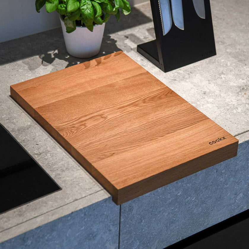 Hackbrett aus Eichenholz, Antirutschkante, hochkant 34 x 50 x 3,5 cm, rechts unten Logo von COOKX eingraviert, Milieubild in Küche, Brett liegt auf Kücheninsel, Ansicht von oben