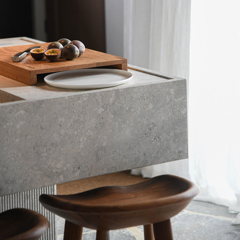 Hackbrett aus Holz Natur, Auffangöffnung für Teller, Milieubild in Küche, weißer Teller in Auffangöffnung, Messer und Früchte liegen auf Brett, Seitenansicht 