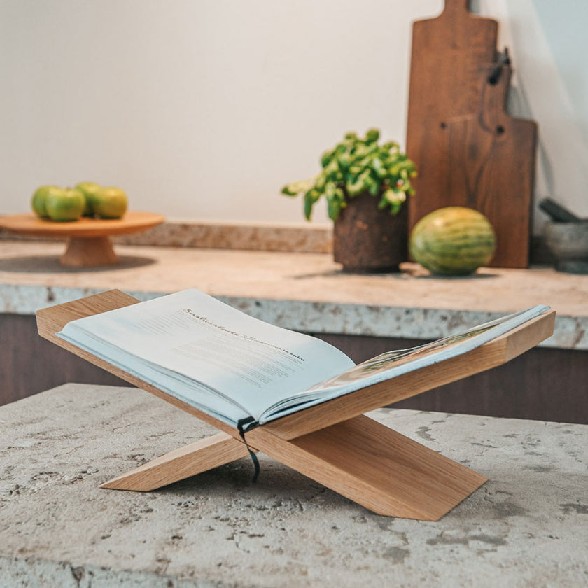 Buchständer aus Eichenholz, x-From, aus zwei gekreuzten Holzelementen, Milieubild frontal auf Arbeitsfläche in der Küche mit Buch