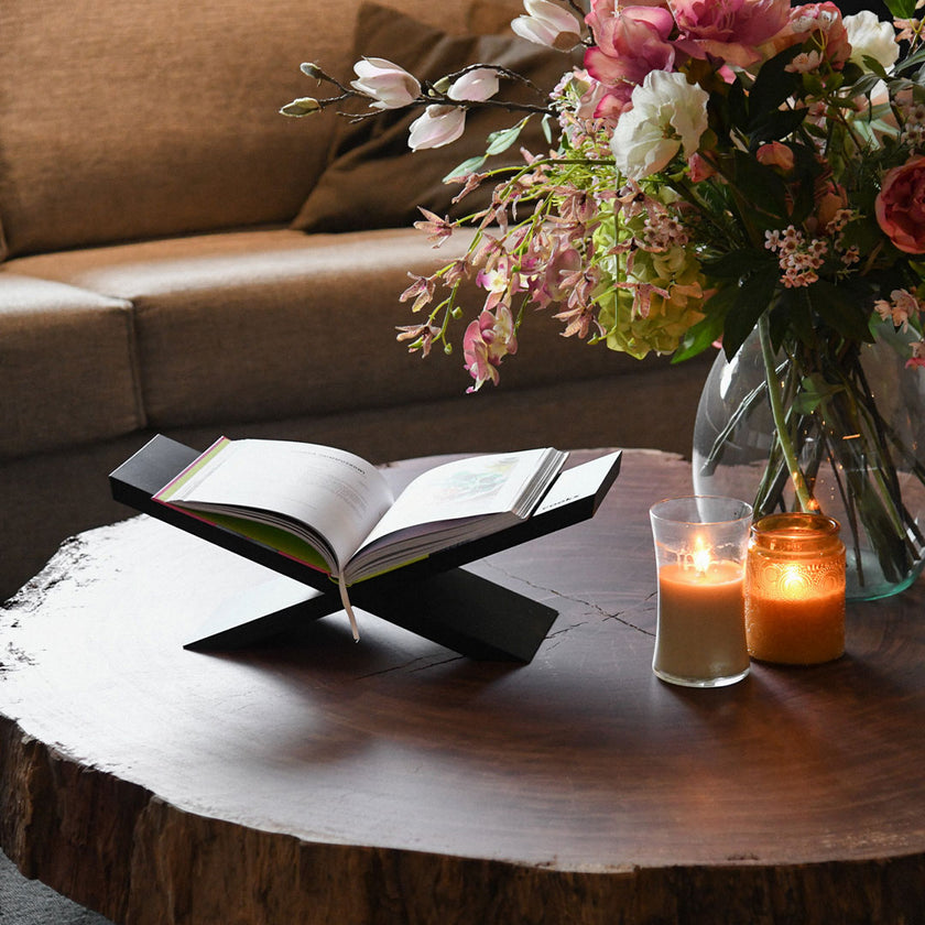 Buchständer aus Eichenholz schwarz, x-From, aus zwei gekreuzten Holzelementen, Milieubild frontal auf Wohnzimmertisch mit Buch