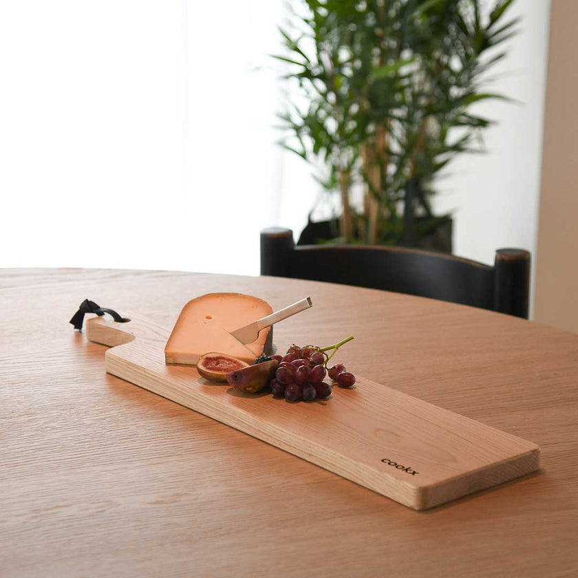 Servierbrett oder Schneidebrett aus Eichenholz Natur mit Griff und schwarzem Lederband zum aufhängen, 800mm x 18mm x 25mm, Milieubild im Esszimmer auf Tisch, Brett mit Käse und Früchten drauf