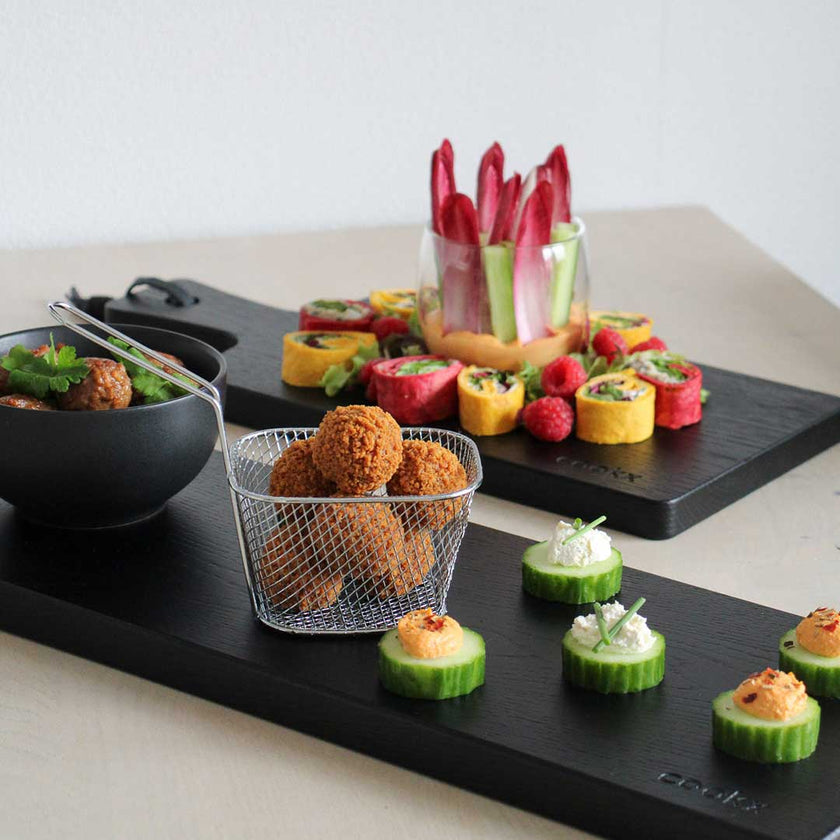 Servierbrett oder Schneidebrett aus Eichenholz schwarz mit Griff und schwarzem Lederband zum aufhängen, 600mmx180mmx25mm, Milieubild in Küche, Servierbrett Größe S und M mit Essen drauf