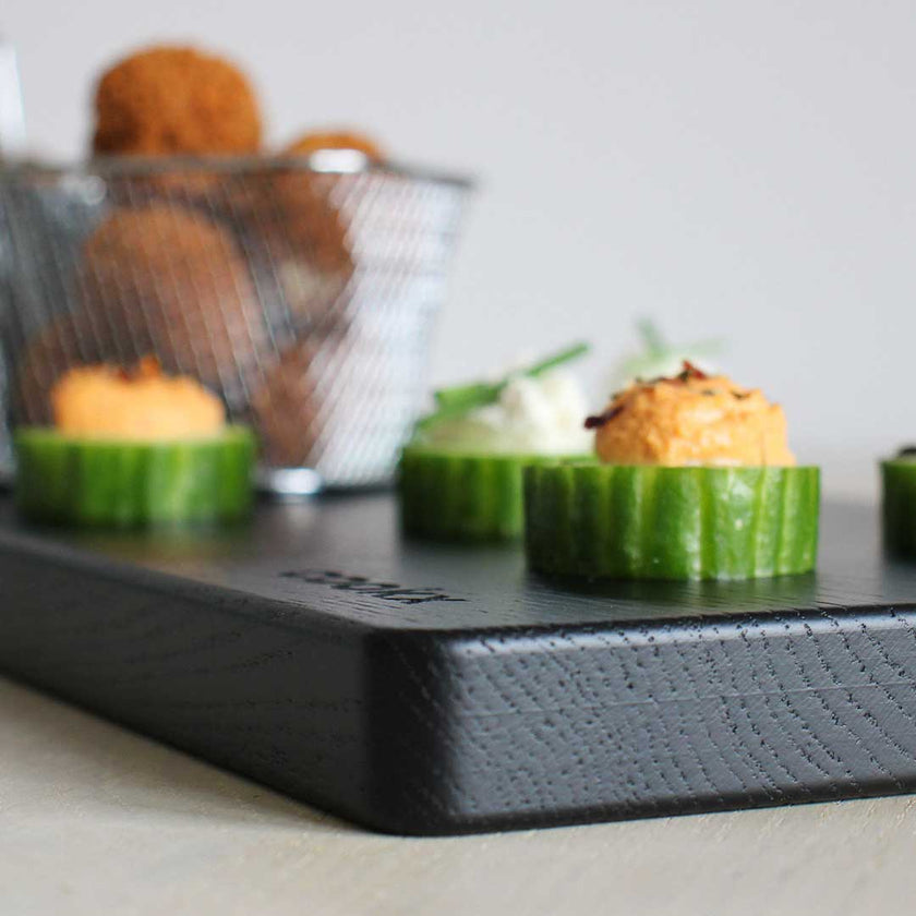 Servierbrett oder Schneidebrett aus Eichenholz schwarz 600mmx180mmx25mm, Milieubild in Küche, Brett mit Essen drauf, Ansicht von einer Ecke aus