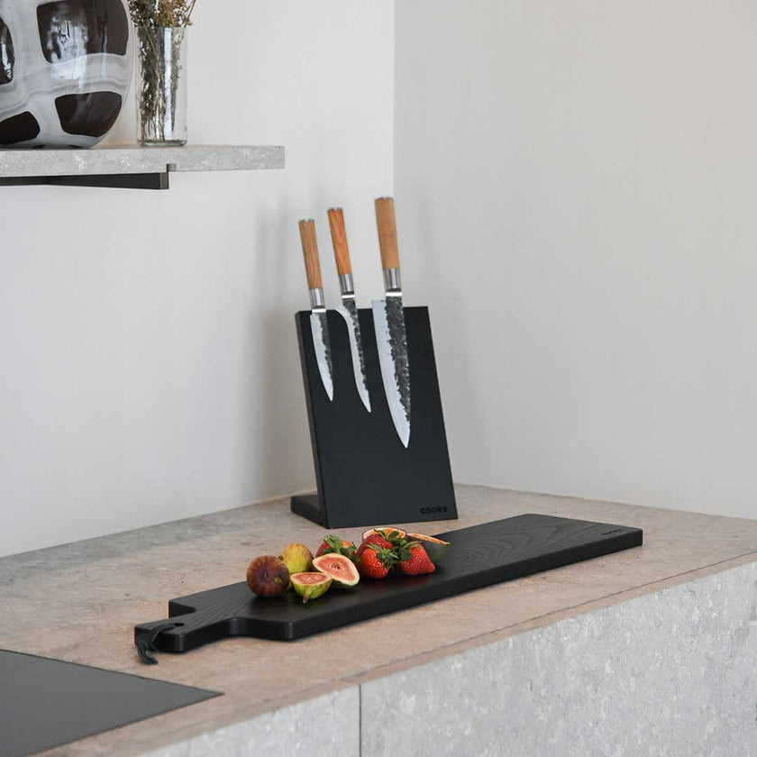 Servierbrett oder Schneidebrett aus Eichenholz schwarz mit Griff und schwarzem Lederband zum aufhängen, 800mmx180mmx25mm, Milieubild in Küche, Brett mit Essen drauf