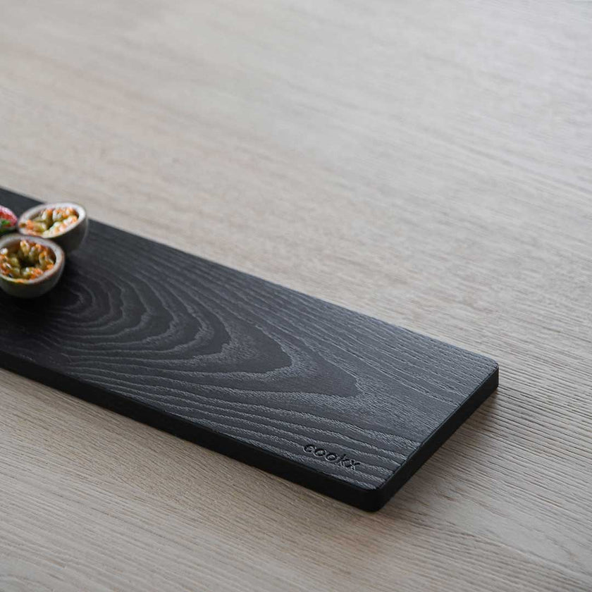 Servierbrett oder Schneidebrett aus Eichenholz schwarz mit Griff und schwarzem Lederband zum aufhängen, 800mmx180mmx25mm, Milieubild im Esszimmer auf Tisch, Ansicht untere Hälfte ohne Griff