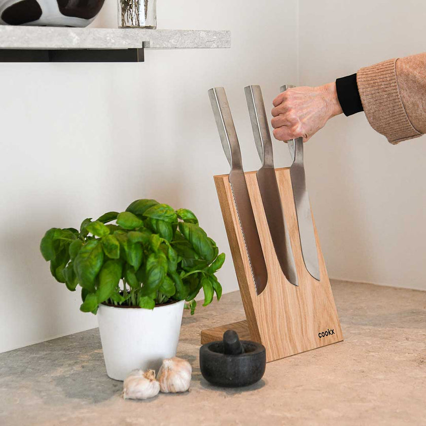 Messerblock aus Eichenholz Natur, magnetisch, Messerblock schräg nach hinten geneigt, Milieubild in Küche, drei Messer am Messerblock, links daneben Basilikumpflanze, ein Messer wird abgenommen 