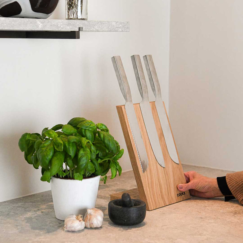 Messerblock aus Eichenholz Natur, magnetisch, Messerblock schräg nach hinten geneigt, Milieubild in Küche, drei Messer am Messerblock, links daneben Basilikumpflanze, Ansicht von links