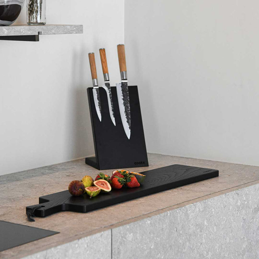Messerblock aus Eichenholz schwarz, magnetisch, Messerblock schräg nach hinten geneigt, Milieubild in Küche, drei Messer am Messerblock 