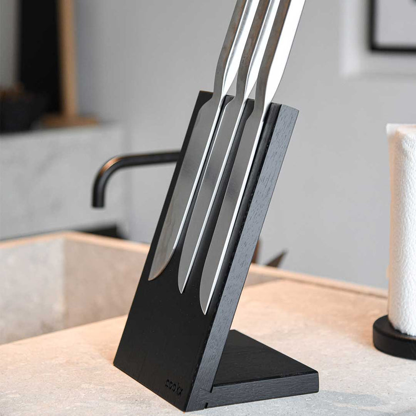 Messerblock aus Eichenholz schwarz, magnetisch, Messerblock schräg nach hinten geneigt, Milieubild in Küche, drei Messer am Messerblock 