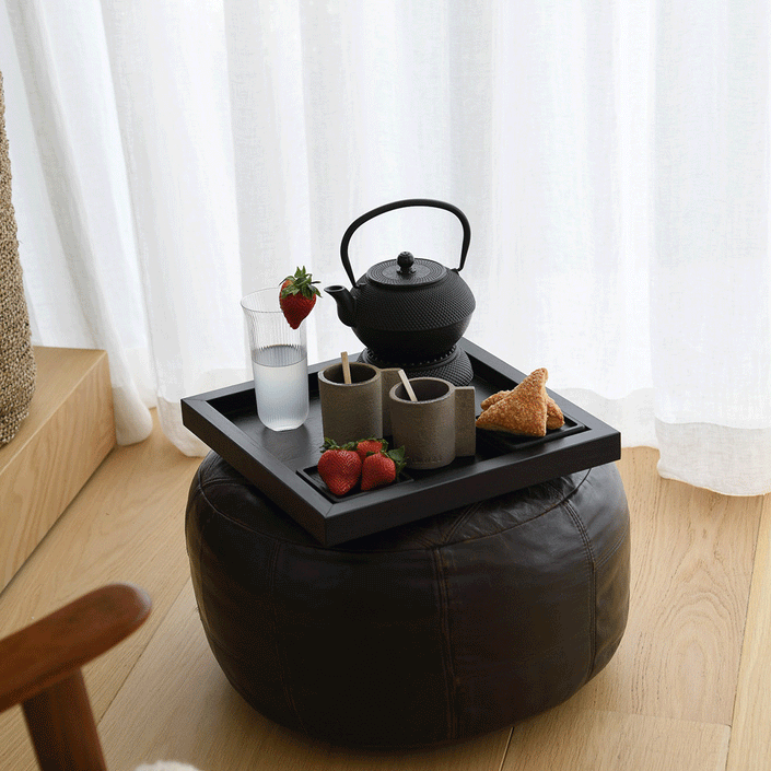 Serviertablett aus Eichenholz schwarz, 40cm x 40cm, Ränder etwas höher, Milieubild im Wohnzimmer, Tablett steht auf Polsterhocker, Gläser stehen auf Serviertablett, Ansicht seitlich   