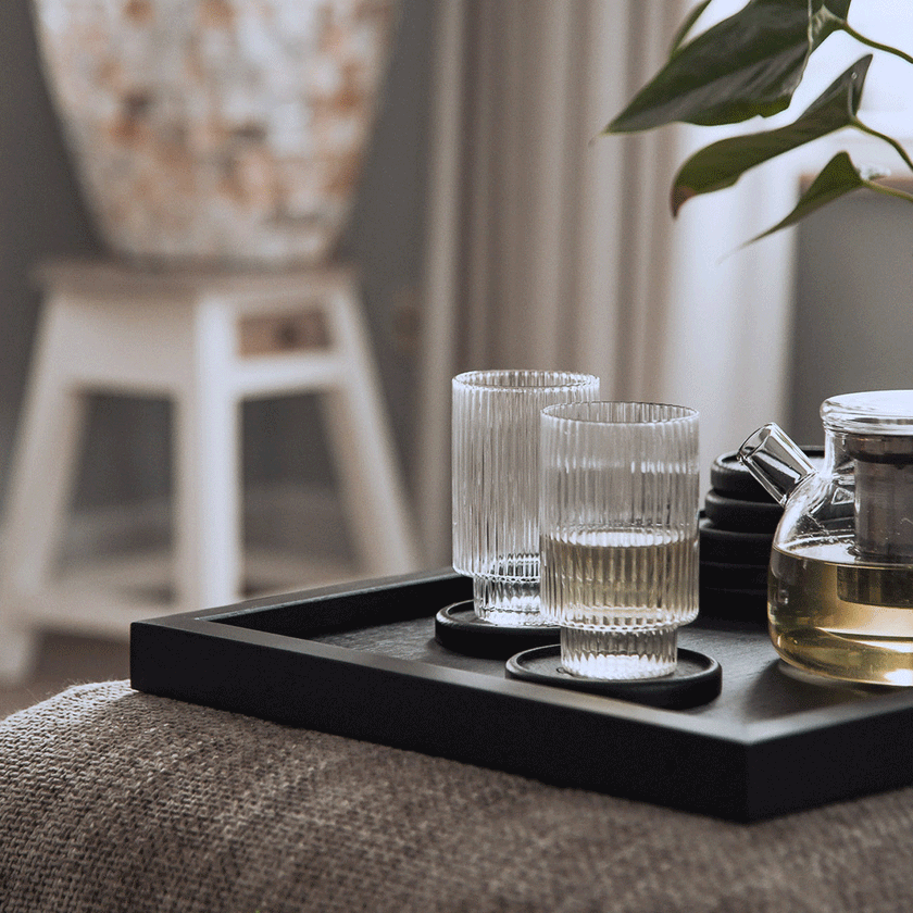 Serviertablett aus Eichenholz schwarz, 40cm x 60cm, Ränder etwas höher, Milieubild im Wohnzimmer, Tablett steht auf Polsterhocker, Gläser stehen auf Serviertablett, Ansicht seitlich   