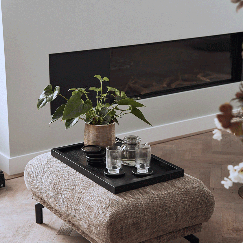 Serviertablett aus Eichenholz schwarz,40cm x 60cm, Ränder etwas höher, Milieubild im Wohnzimmer, Tablett steht auf Polsterhocker, Gläser und Pflanze stehen auf Serviertablett, Ansicht seitlich   