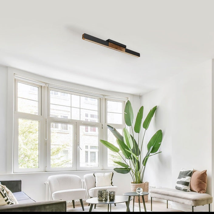 Deckenleuchte aus Asteiche geölt, Modell Lana del nero, 1000mm, Kopfholz, schwarze Applikationen, LED, Klick & Dimm, Milieubild im Wohnzimmer, Leuchte hängt an Decke über Sofa und Sessel