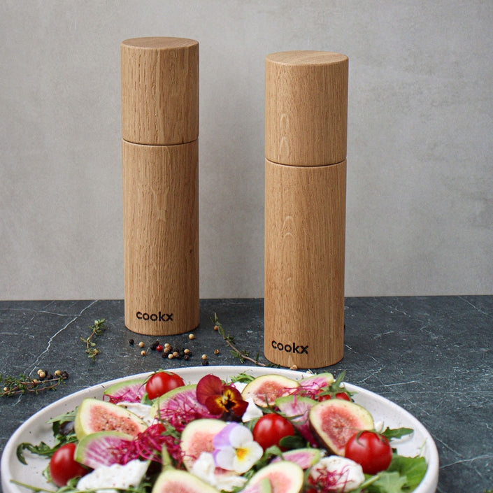 Salz-/Pfeffermühle Set aus Eichenholz Natur, 23cm hoch, Milieubild in Küche, Set steht hinter Teller mit Salat. Frontalansicht