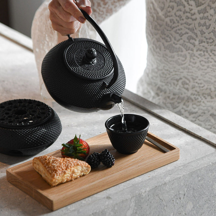 Kerzentablett aus Eichenholz schwarz,  28 x 14 x 2,3 cm, Milieubild in Küche, auf Tablett liegen Gebäck, Früchte und kleine schwarze Tasse, Wasser von Teekanne in Tasse geschüttet