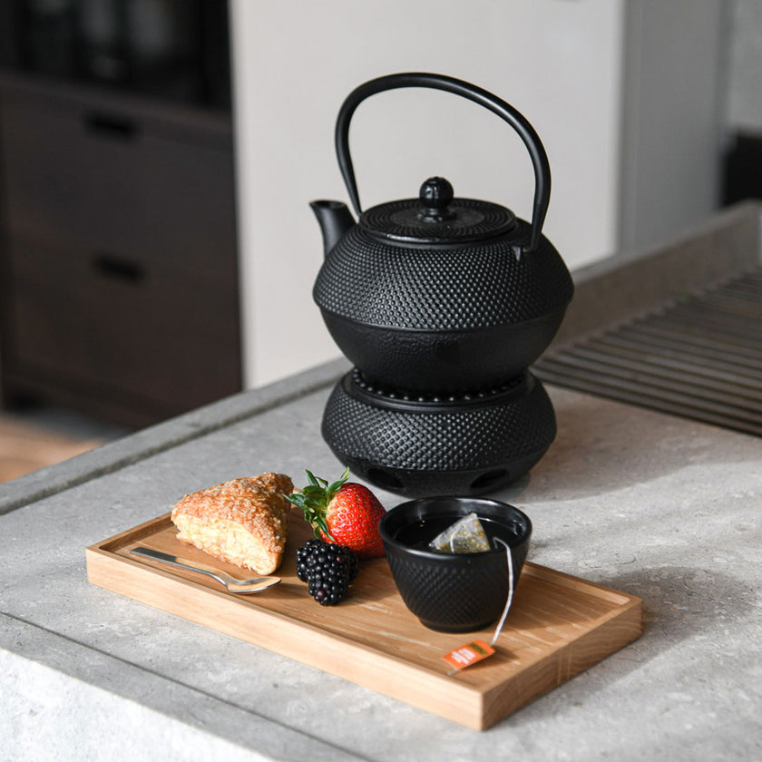 Kerzentablett aus Eichenholz schwarz,  28 x 14 x 2,3 cm, Milieubild in Küche, auf Tablett liegen Gebäck und Früchte, Löffel und kleine schwarze Schüssel mit Teebeutel, im Hintergrund steht Teekanne 