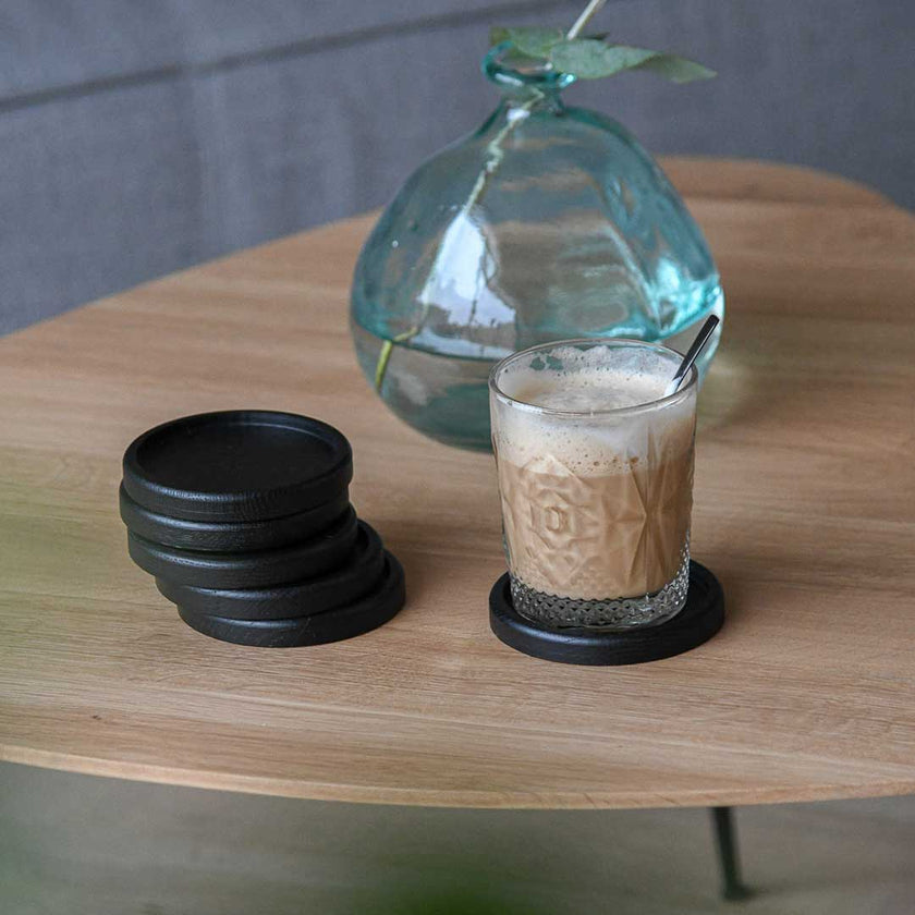 Untersetzer aus schwarzer Eiche, 6 Stück, 10cm Durchmesser, sind auf einem Wohnzimmertisch, ein Kaffee steht auf einem der Untersetzer, Ansicht von vorne