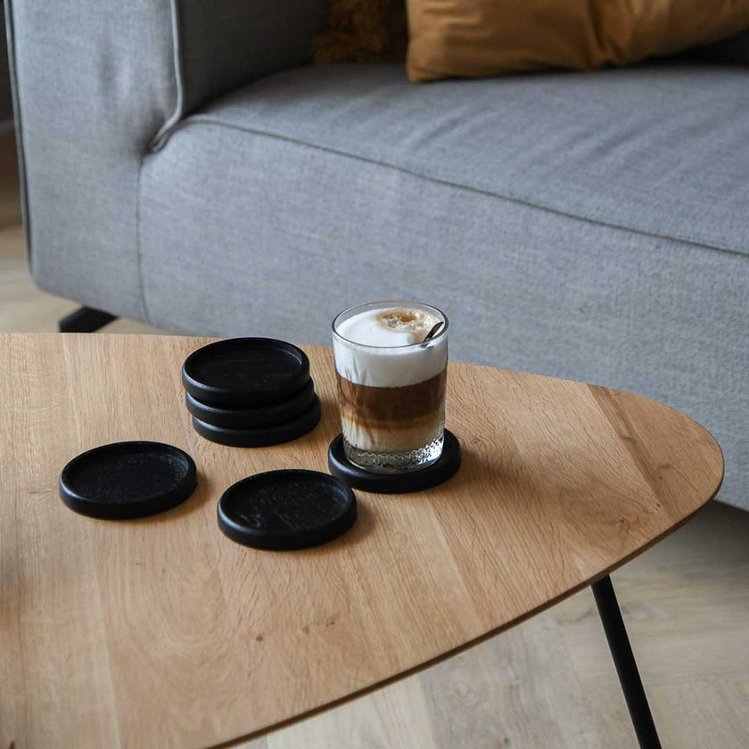 Untersetzer aus schwarzer Eiche, 6 Stück, 10cm Durchmesser, die Untersetzer liegen auf einem Wohnzimmertisch, ein Kaffee steht auf einem der Untersetzer, Ansicht von der Seite